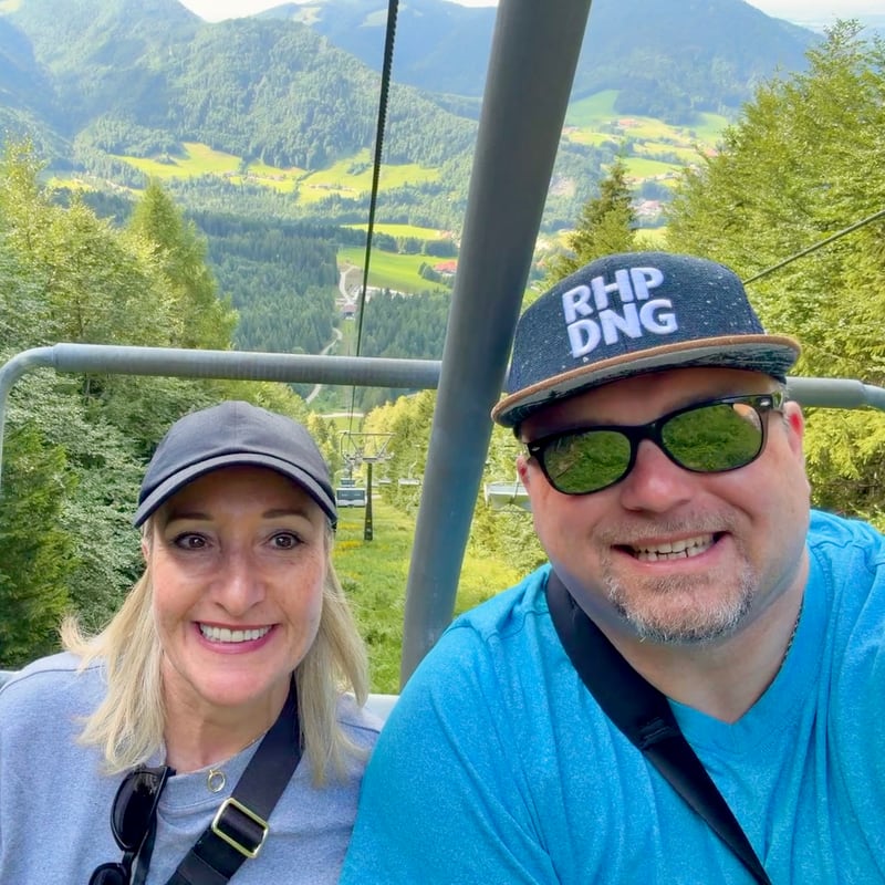 Christoph and Steffi smiling on a chairlift, a green Alpine valley behind them