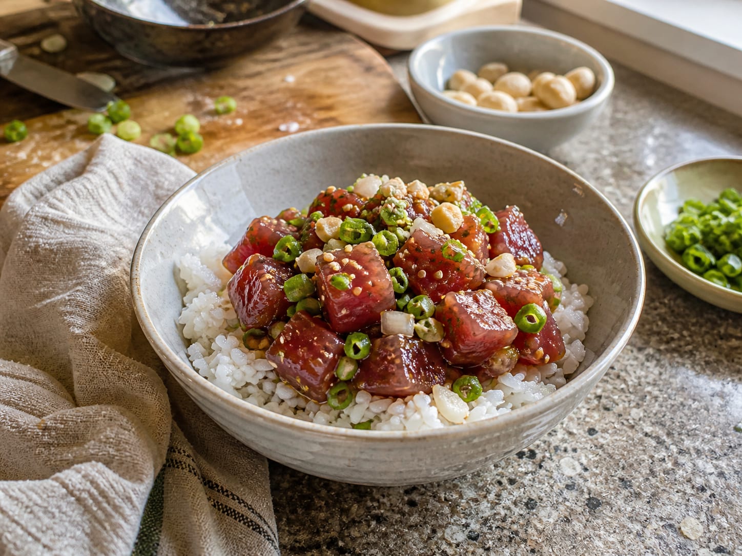 A bowl of cubed raw ahi tuna poke over warm rice, topped with sliced scallion, sweet onion and chopped macadamia nuts