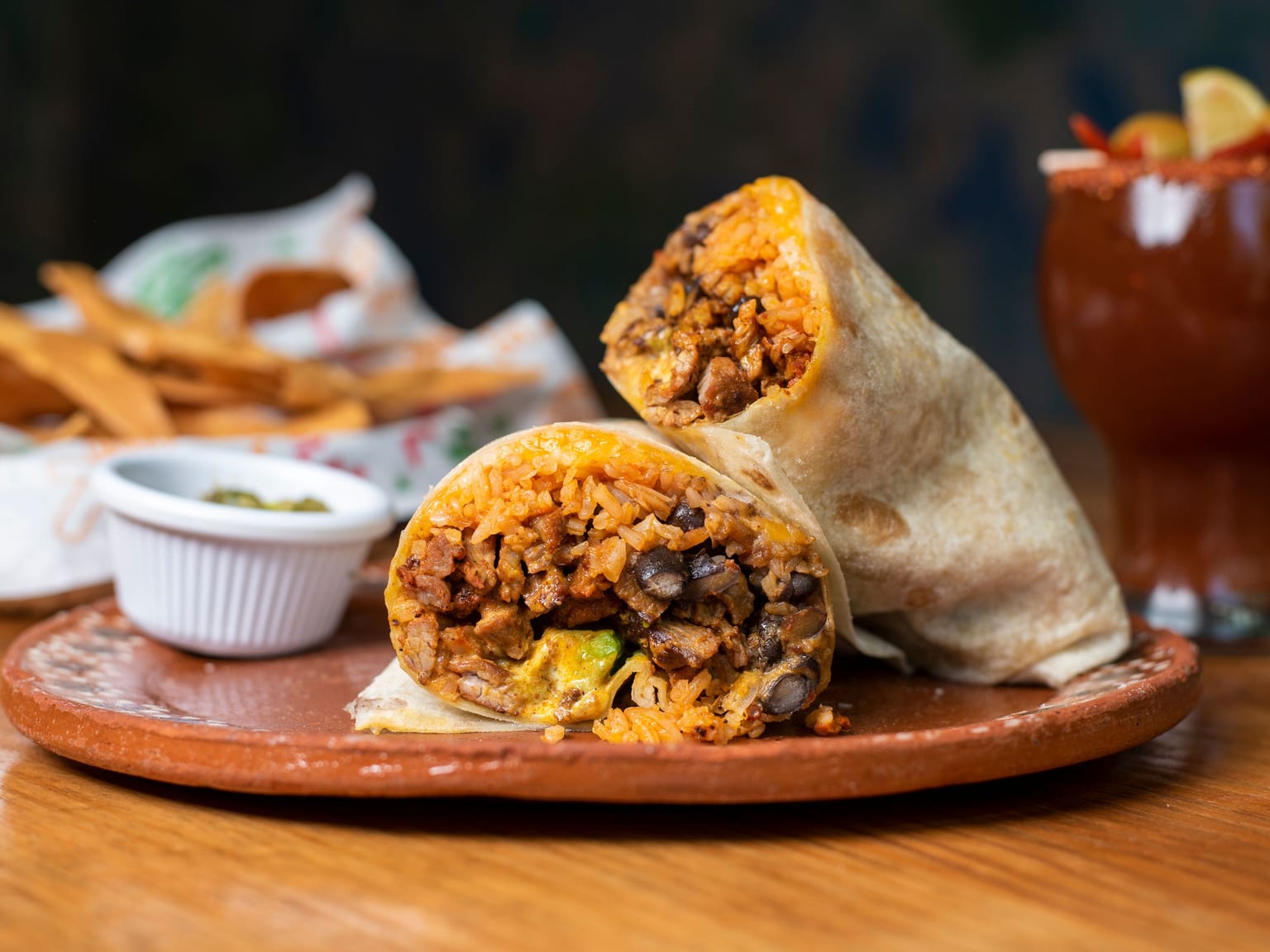 Two toasted burrito halves showing ground beef, pinto beans, rice, and melted cheddar, with lettuce, tomato, sour cream, and guacamole alongside