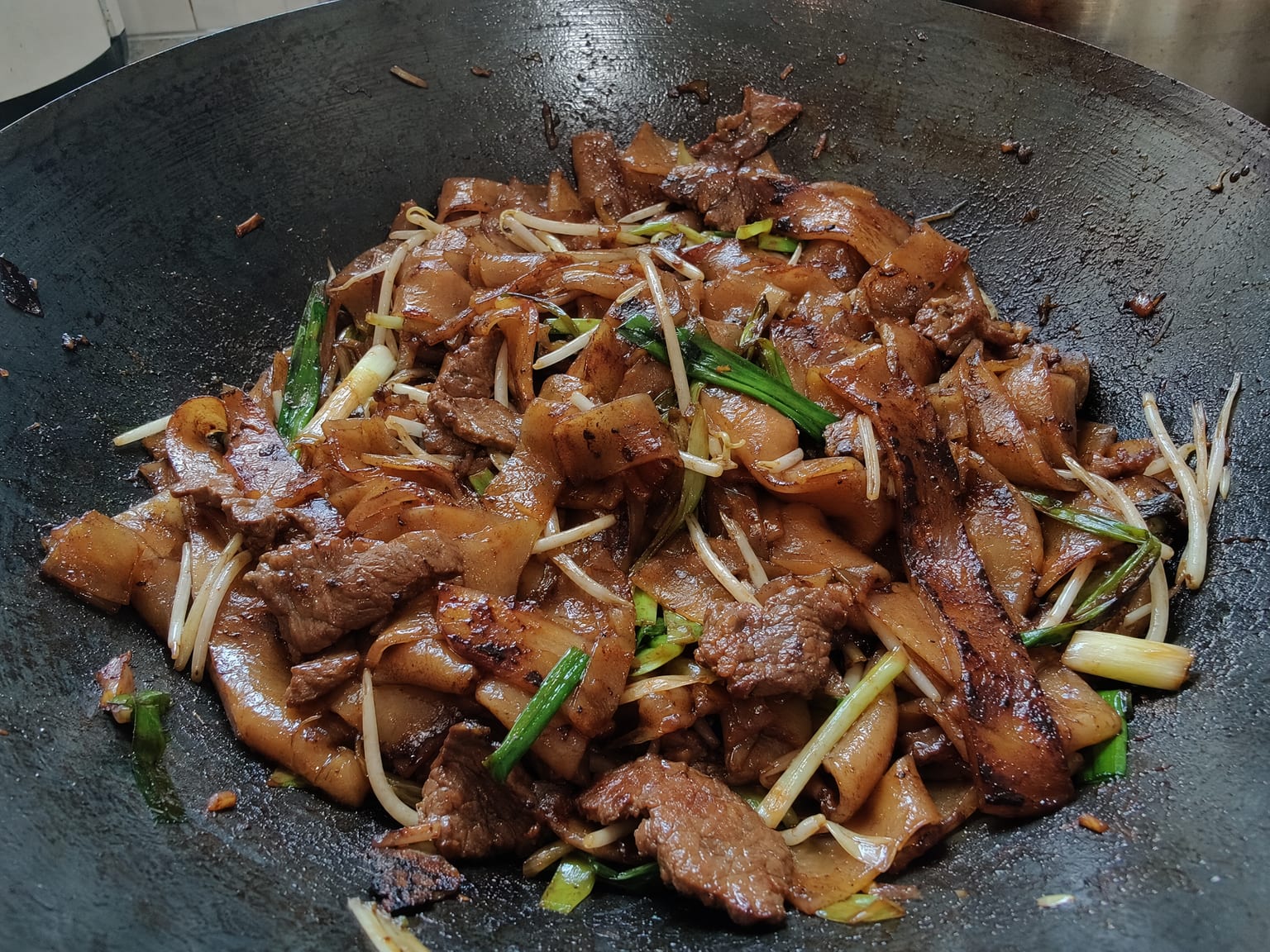 Wide flat rice noodles with sliced beef and bean sprouts, glossy dark and slightly charred