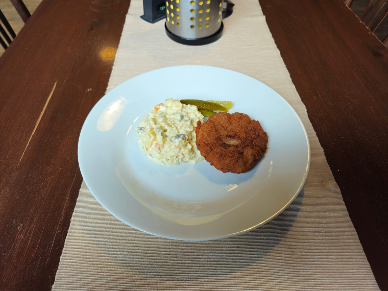 Six flat deeply browned beef Frikadellen in a pan on a cream surface, a green side salad beside them in natural light