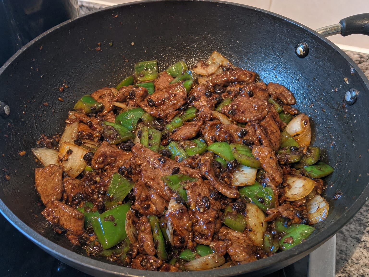 Sliced beef with green pepper and onion squares in a glossy dark black bean sauce