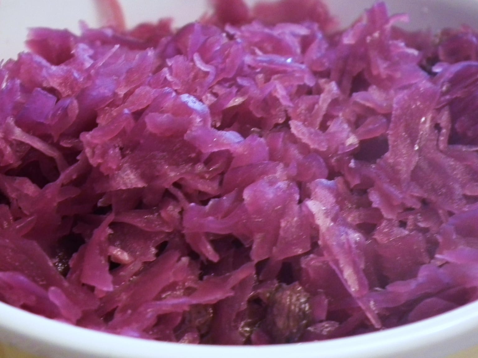 Dark glossy braised red cabbage heaped in a cream bowl, a bay leaf on the rim, natural light from the left