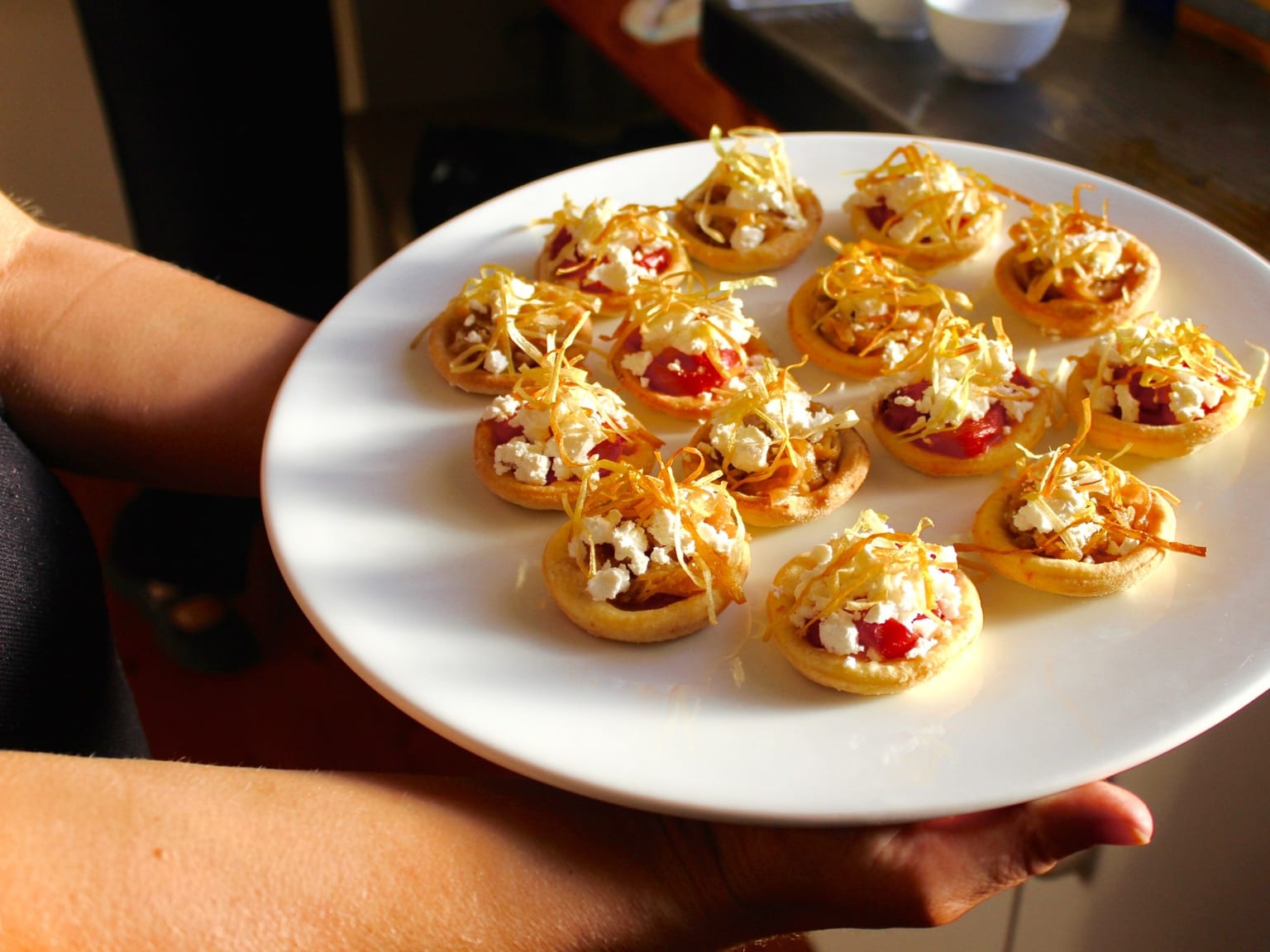 Caramelised onion, feta, and thyme puff tartlets served as a natural-light editorial food photograph