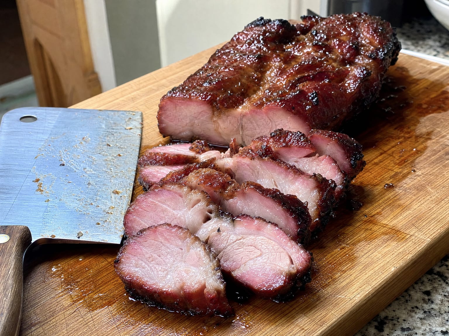 Sliced char siu pork with lacquered dark red edges on a board, showing a pink-tinged interior