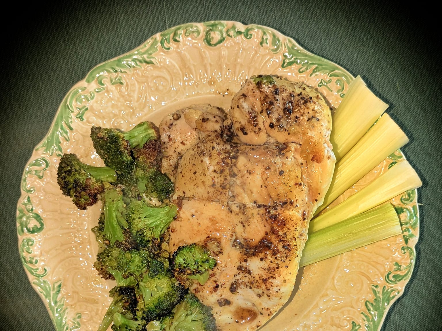 Sliced golden chicken breast beside browned broccoli florets on a cream plate in natural light