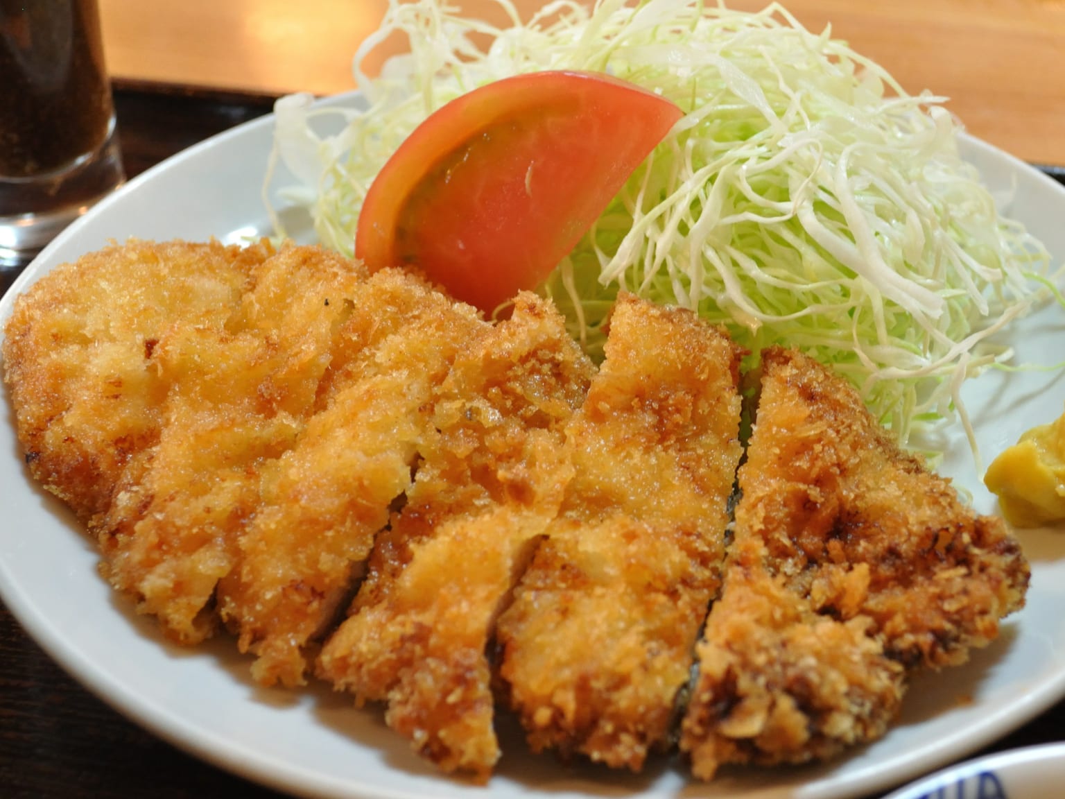 Sliced panko-crusted chicken katsu on a cream plate in natural light, a mound of finely shredded cabbage beside it, dark tonkatsu sauce in a small dish