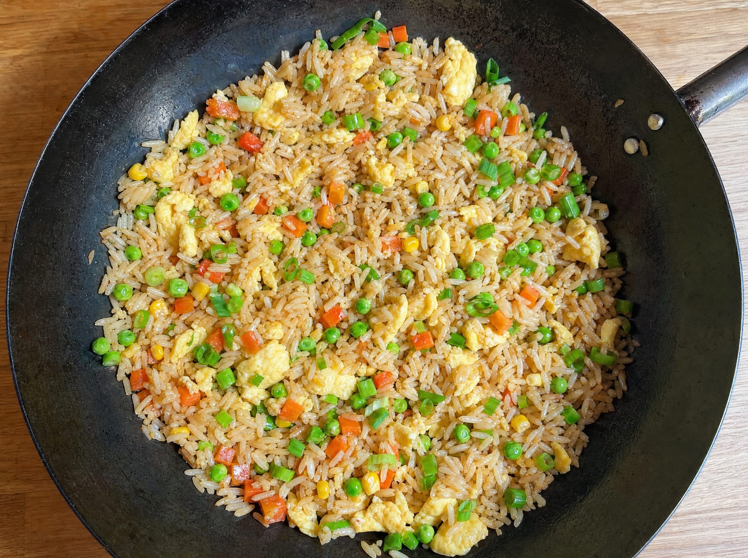 A wok of fried rice with separate glossy grains, egg, peas, carrot and scallions