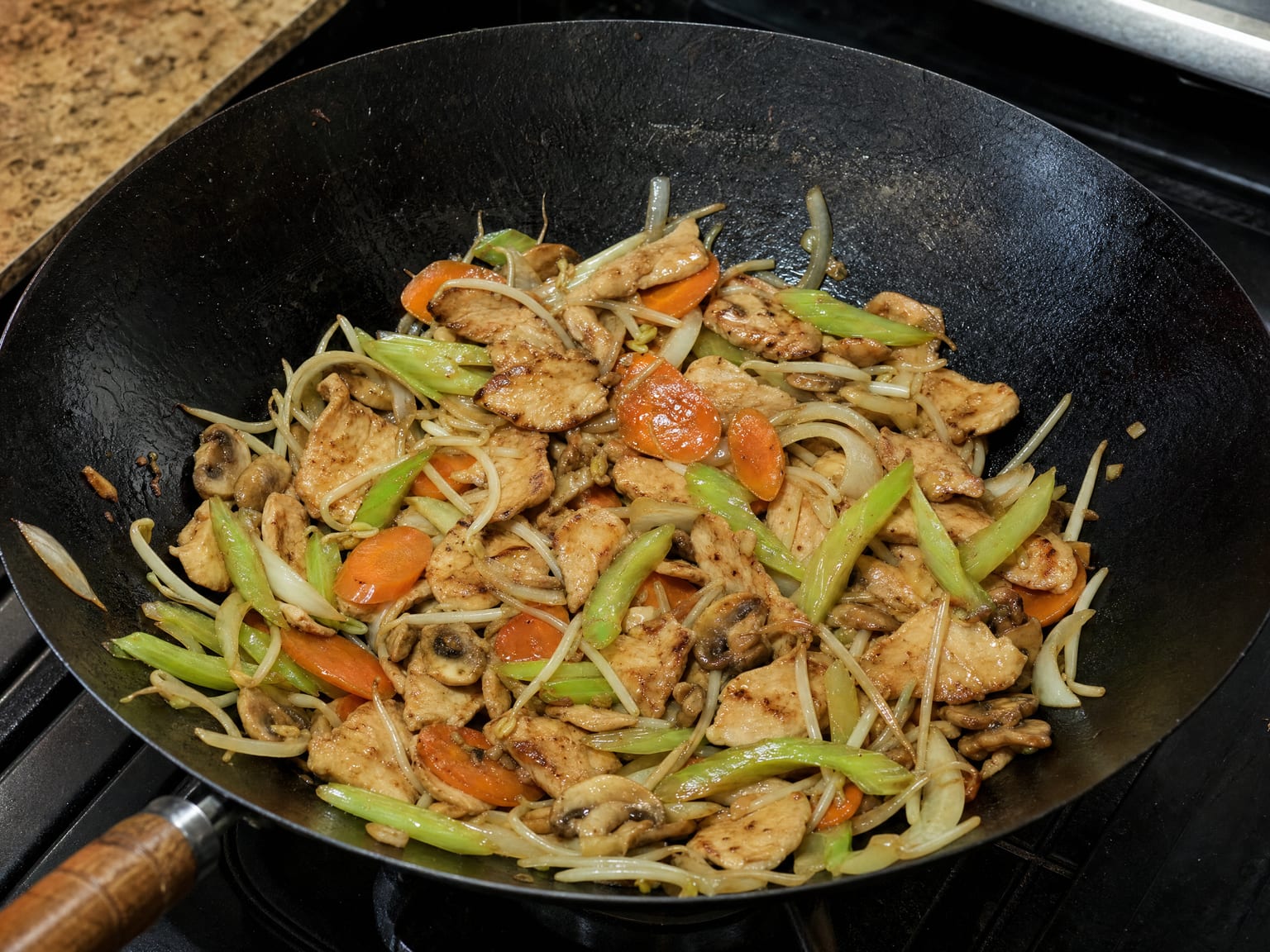 A wok of chop suey with glossy sauce coating sliced chicken, celery, carrot, mushrooms and bean sprouts