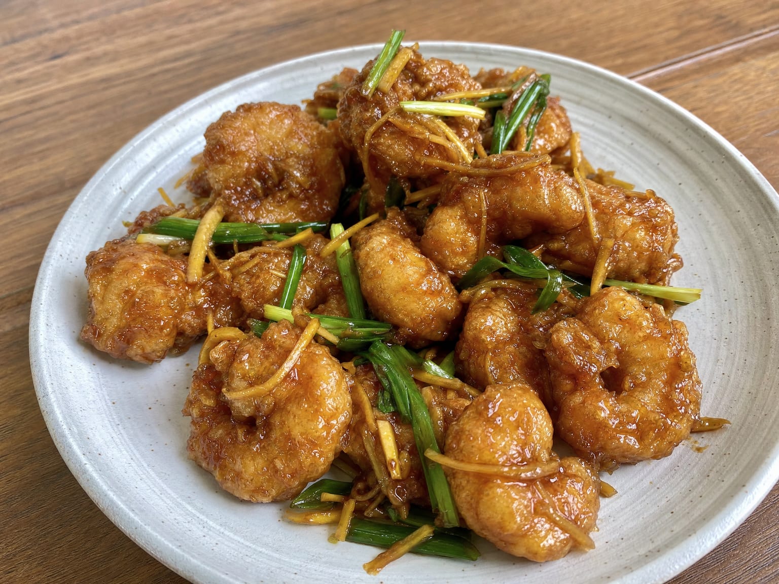 Crisp battered prawns in a sticky dark ginger sauce with visible ginger matchsticks and scallions