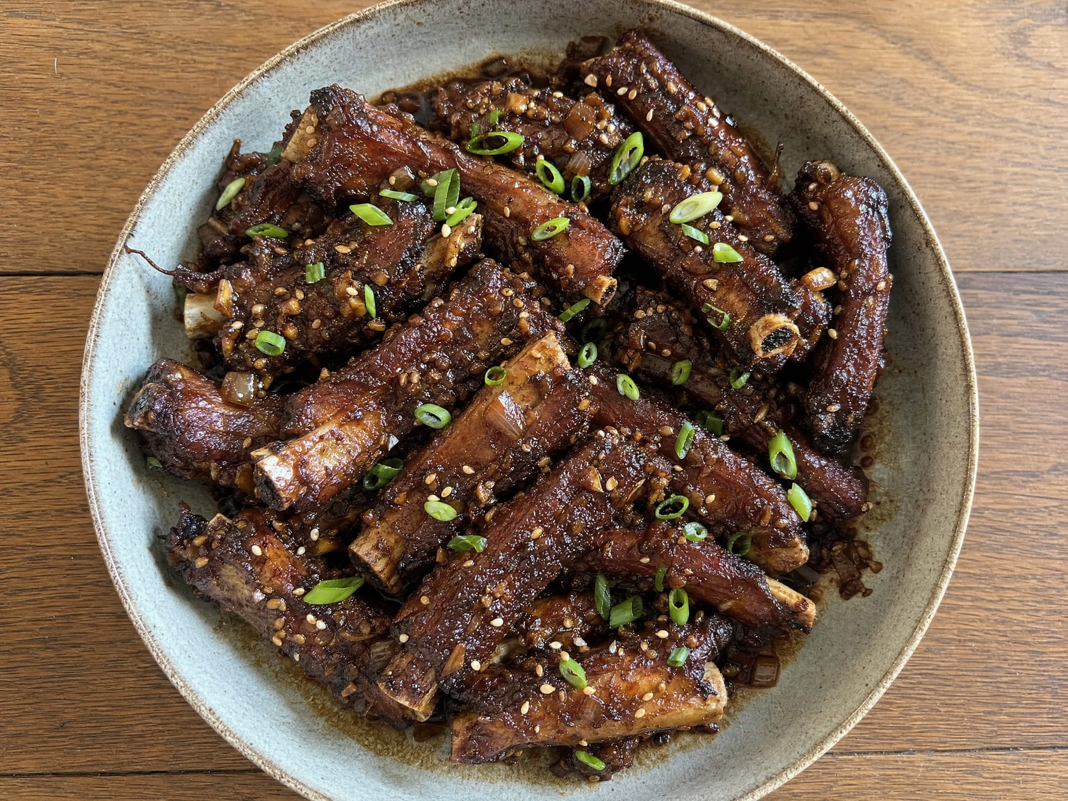 Dark braised dry garlic ribs glossy with reduced sauce and scattered with scallions and sesame