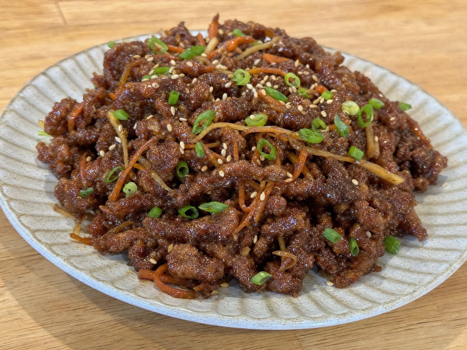 A plate of crispy shredded ginger beef in sticky dark sauce with julienned carrot and scallions