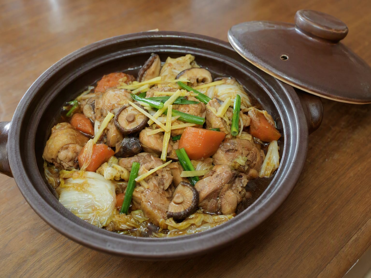 A clay pot of chicken braised with carrot, napa cabbage and shiitake in a dark glossy ginger sauce
