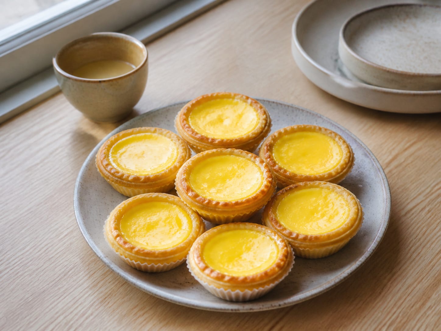 Twelve golden Hong Kong egg tarts in fluted shortcrust shells cooling on a wire rack, pale yellow custard visible from above on the nearest tart