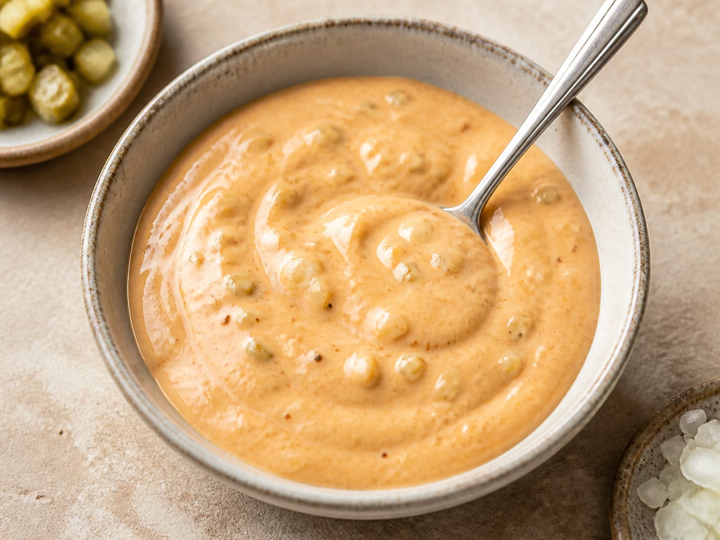 A small bowl of pale orange burger sauce dotted with finely chopped dill pickle
