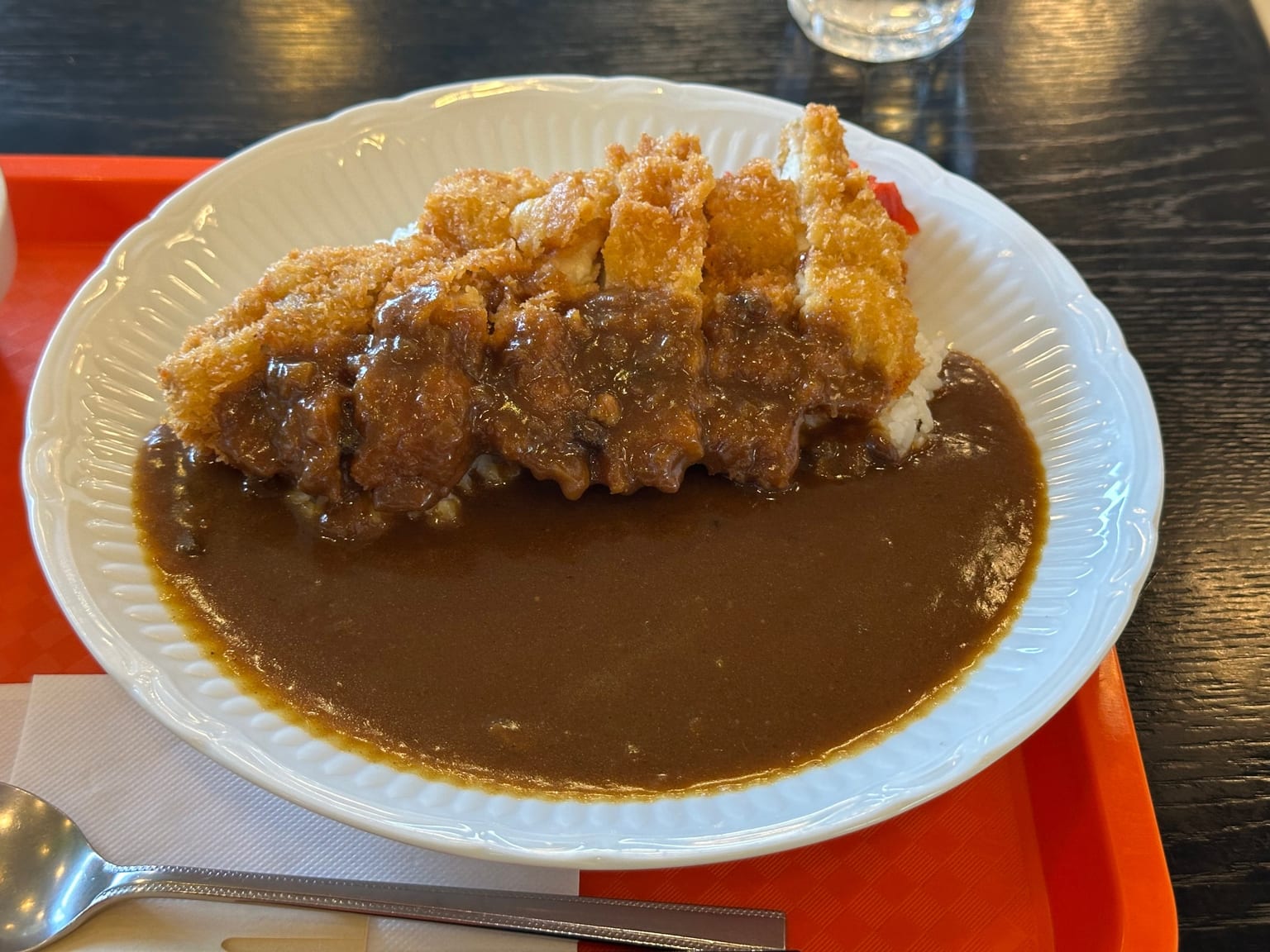 A cream bowl with steamed rice on one side, sliced panko chicken katsu leaning against it, thick brown Japanese curry poured alongside, a small heap of red pickle at the edge