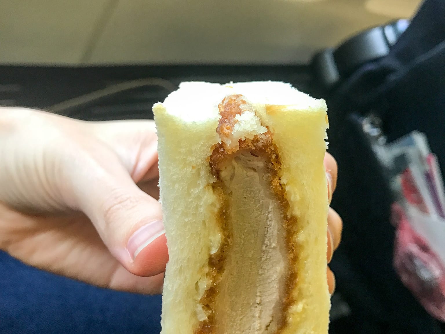 Two halves of a katsu sando standing cut side up on cream paper, crusts trimmed, the panko cutlet and dark sauce showing in cross section