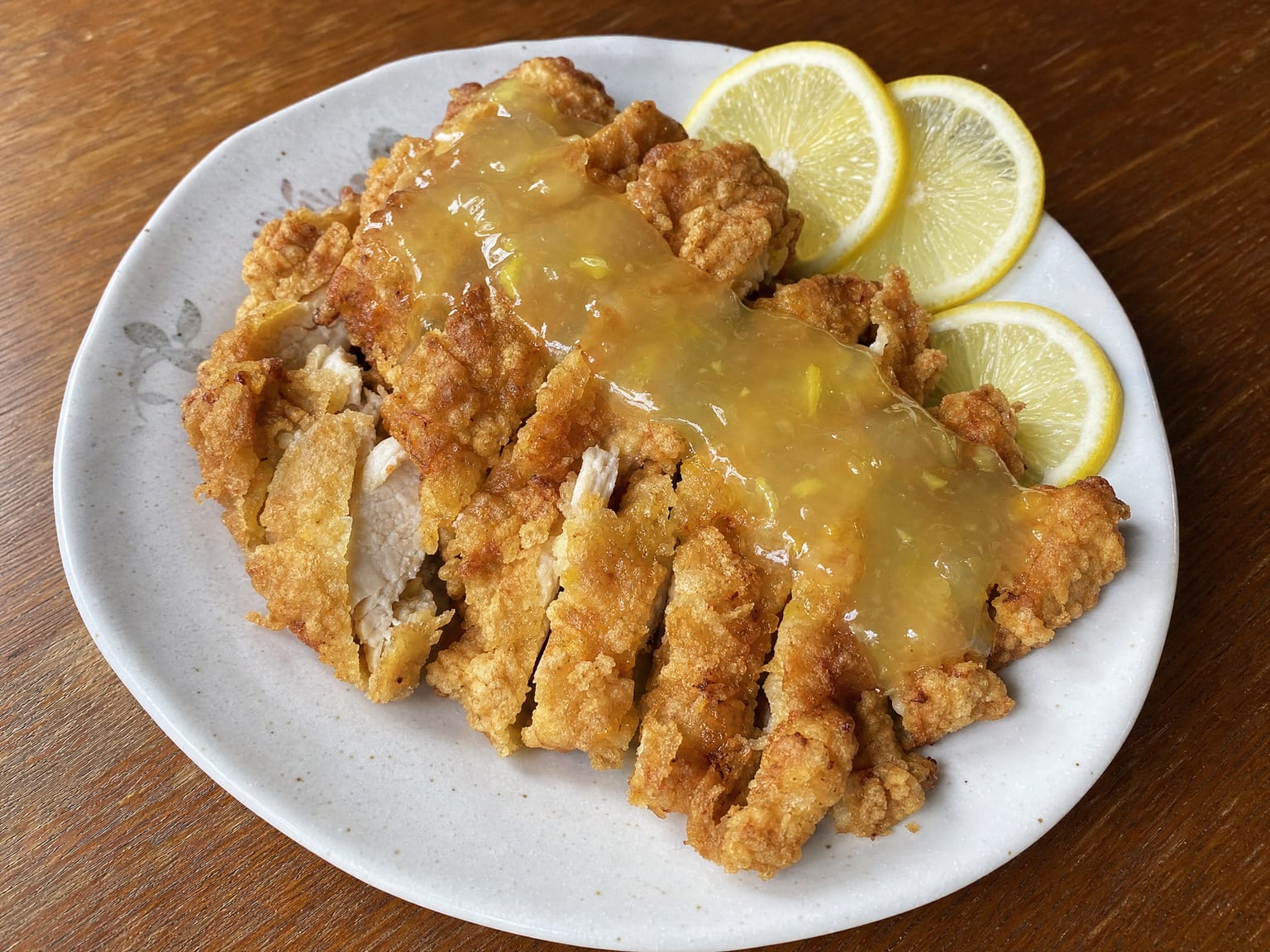 Sliced crisp battered chicken under a clear glossy yellow lemon sauce with lemon slices
