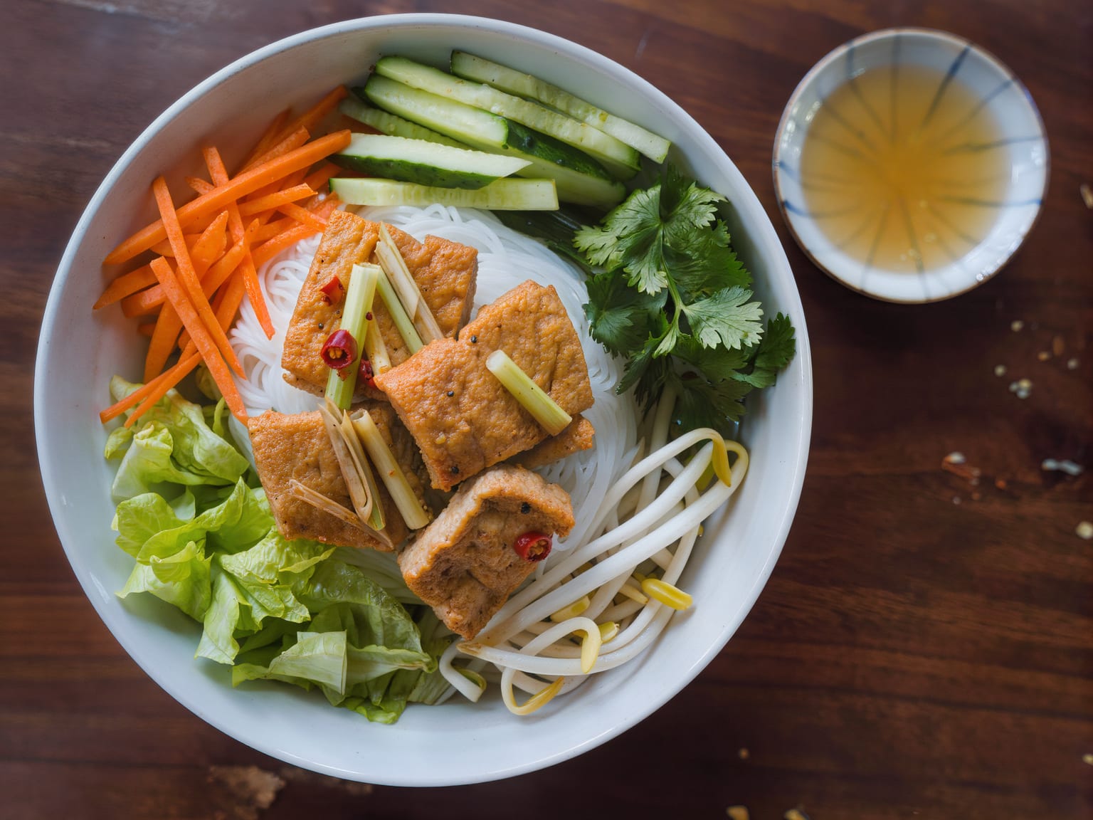 A vermicelli bowl with golden lemongrass tofu, pickled carrot, cucumber, herbs and a dish of dipping sauce
