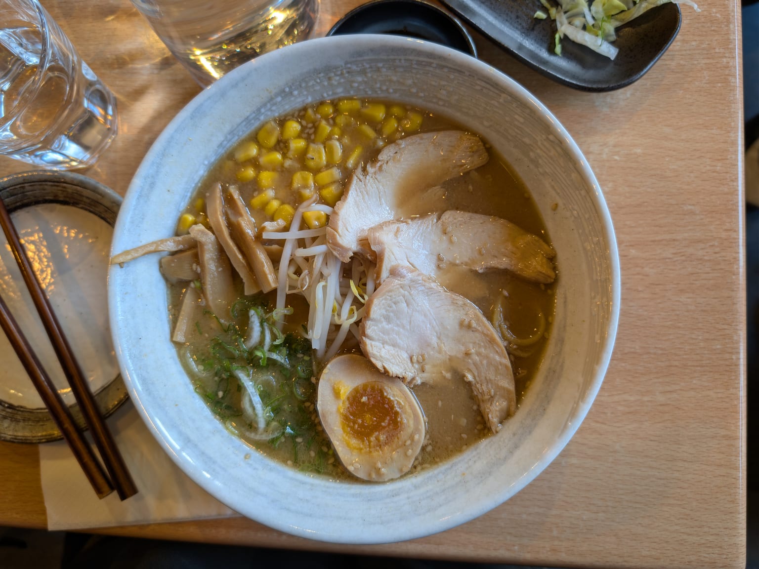 A bowl of miso ramen with ground pork, corn, a halved soft egg and sliced scallions in a cloudy broth