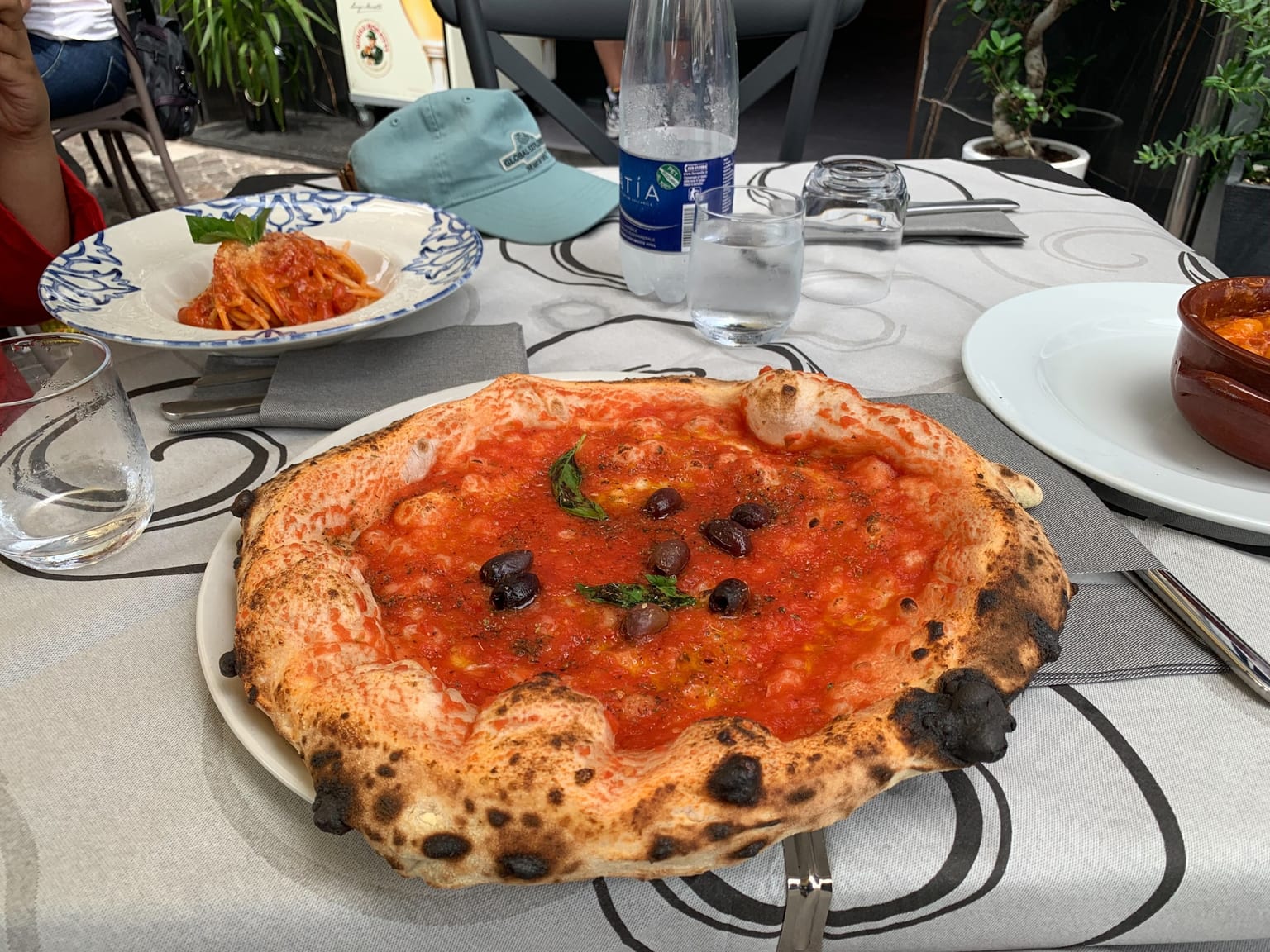 A Neapolitan pizza on a wooden peel in natural light, thin centre under torn mozzarella and basil, puffed rim spotted dark from the oven floor