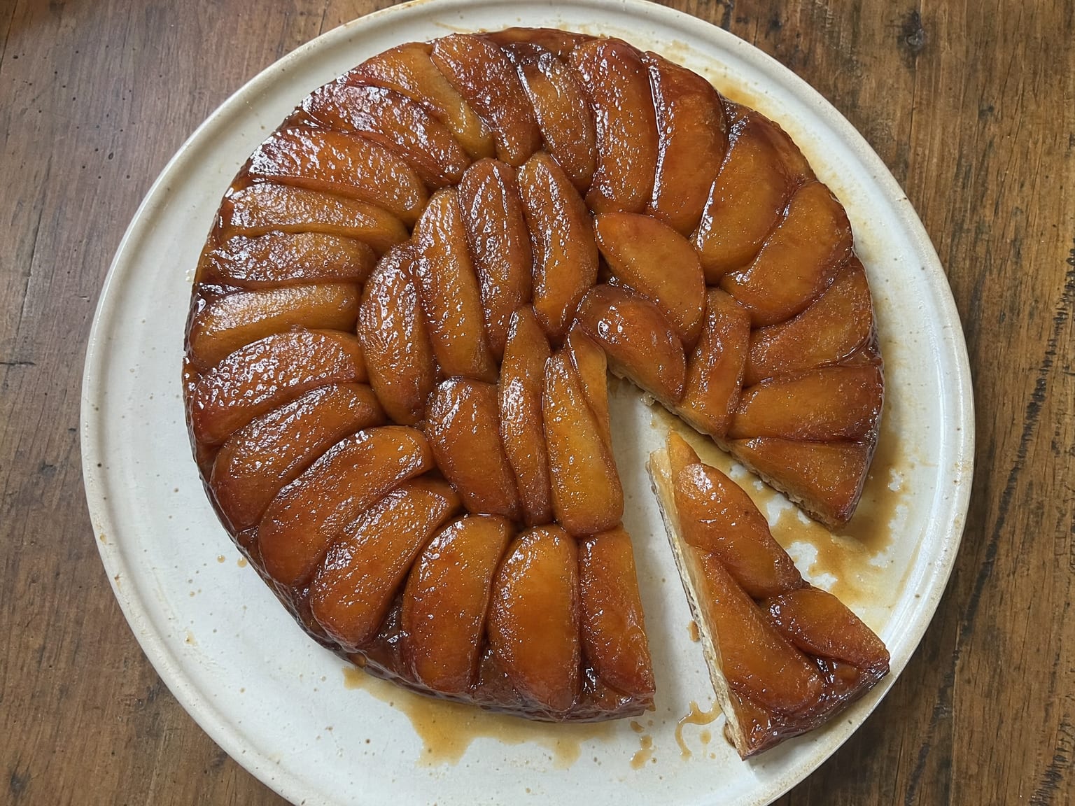 A quick apple tarte tatin flipped onto a plate with glossy caramelized apple slices on top