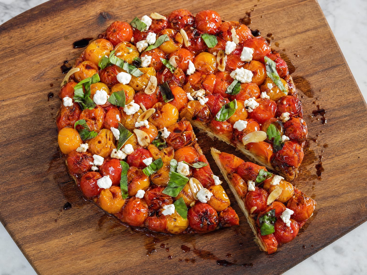 A savoury cherry tomato tarte tatin flipped onto a board, glossy burst tomatoes scattered with basil