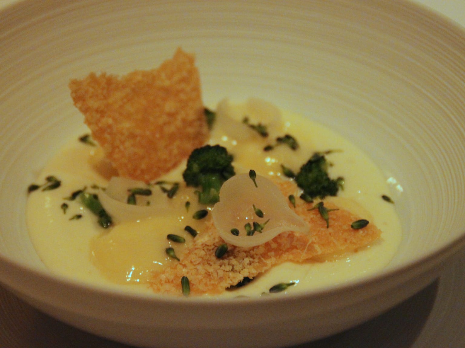 Pale ricotta gnudi in a shallow cream bowl in natural light, coated in brown butter with crisp dark sage leaves and a dusting of grated parmesan