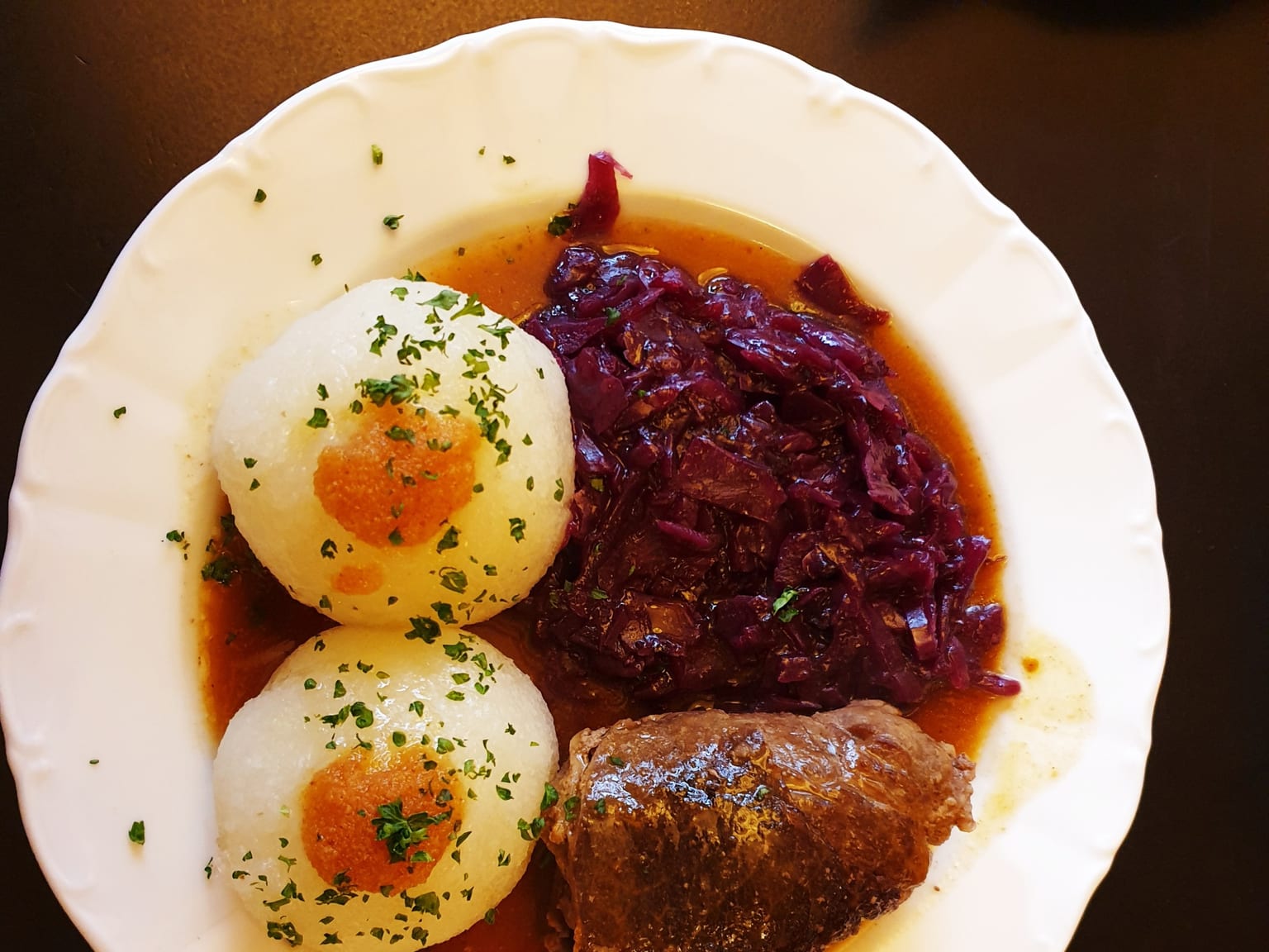 Two beef rouladen on a cream plate under a dark red wine sauce, kitchen twine removed, parsley scattered over, natural light from the side