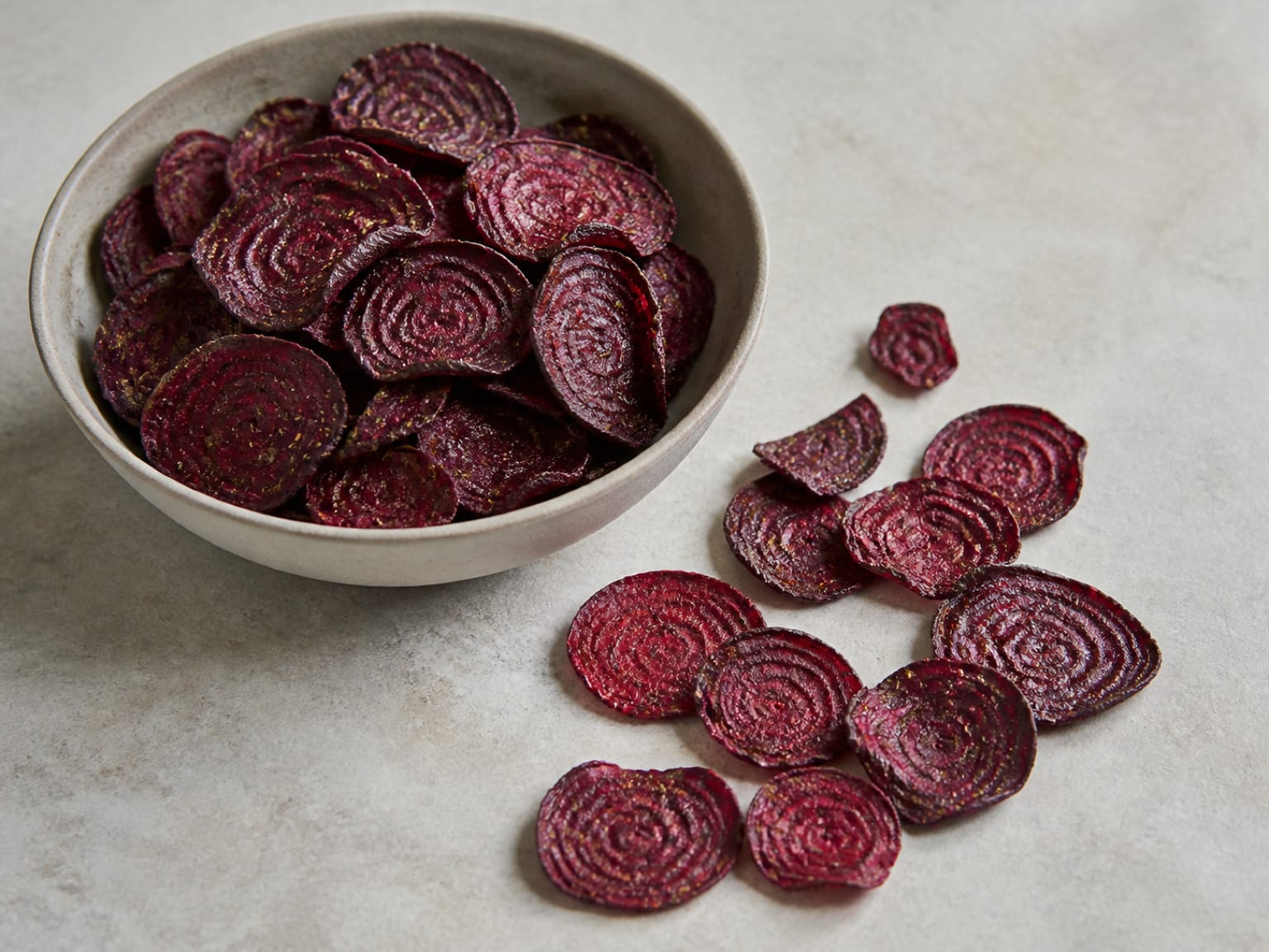 Tief rubinrote Rote-Bete-Chips mit gewellten Rändern und einer feinen Rosmarinschicht