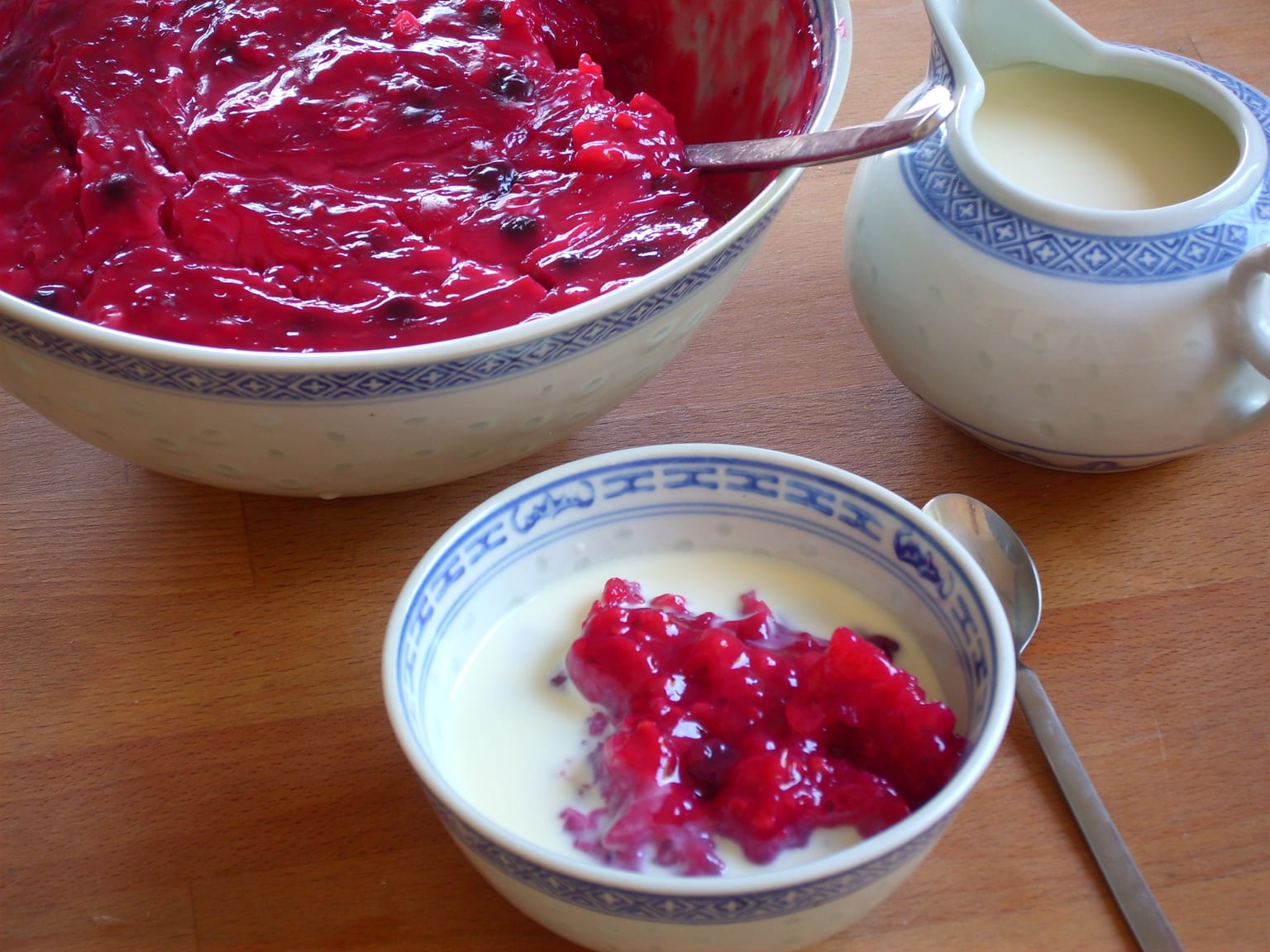 Rote Grütze in a shallow cream bowl, dark red and glossy with whole berries visible, vanilla sauce poured over one side, natural light