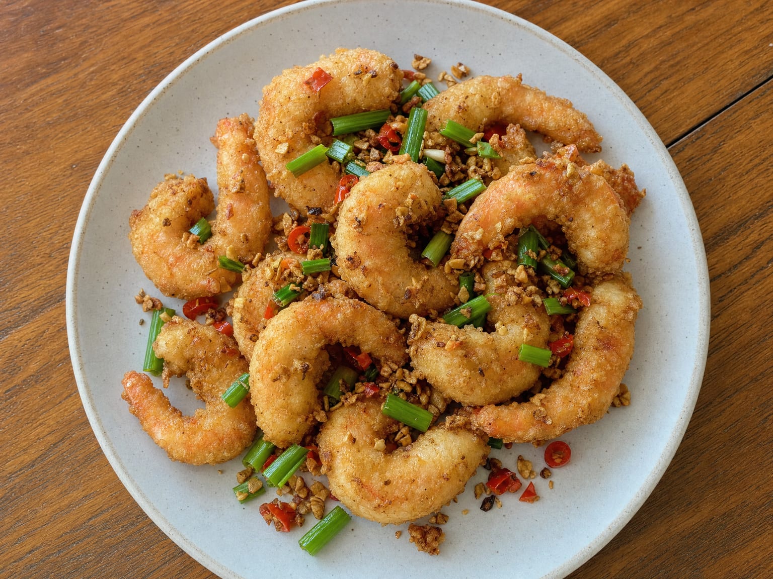 Crisp salt and pepper prawns tossed with chopped garlic, red chilli and scallions on a plate