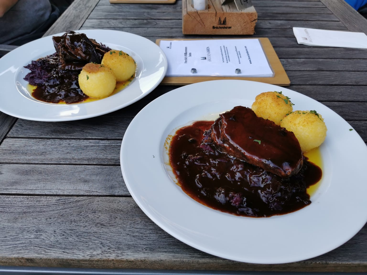Sliced Sauerbraten on a cream platter under a dark glossy raisin sauce, natural light from the side