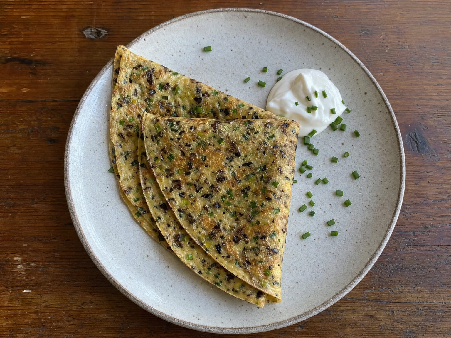 A savoury herb pancake flecked with mushroom, leek and chives, folded on a plate
