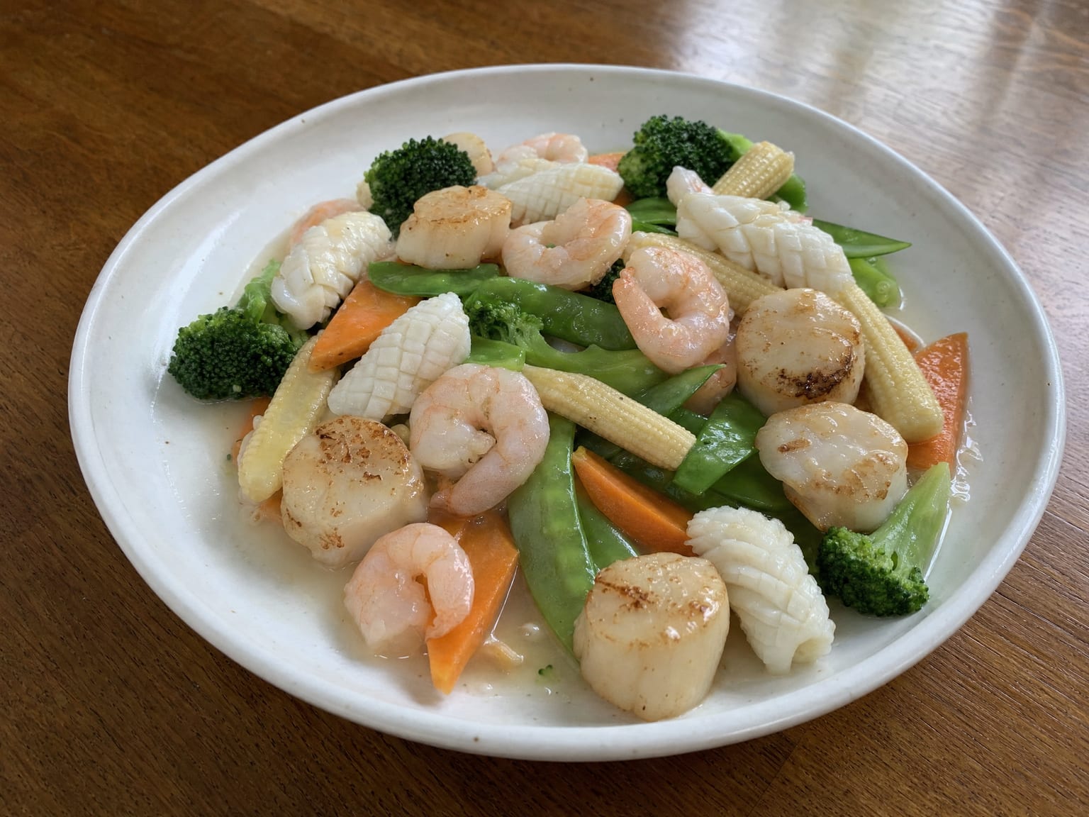 Prawns, squid and scallops with broccoli, carrot and snow peas in a pale glossy sauce