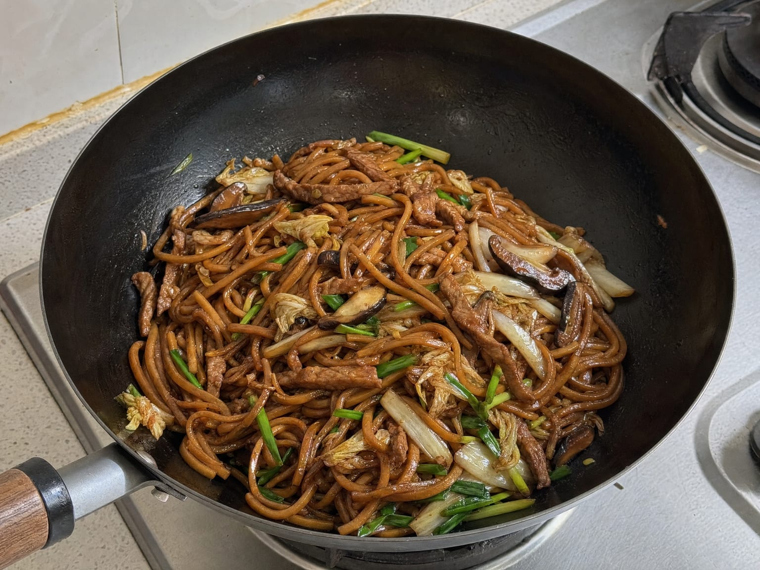 A wok of thick dark brown Shanghai noodles with pork strips, shiitake and napa cabbage