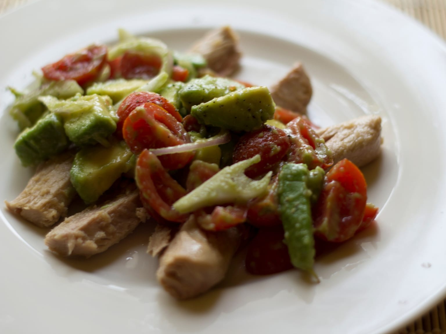 A wide plate of salad greens with flaked tuna and fanned avocado slices, olive oil and a lemon half beside it in daylight