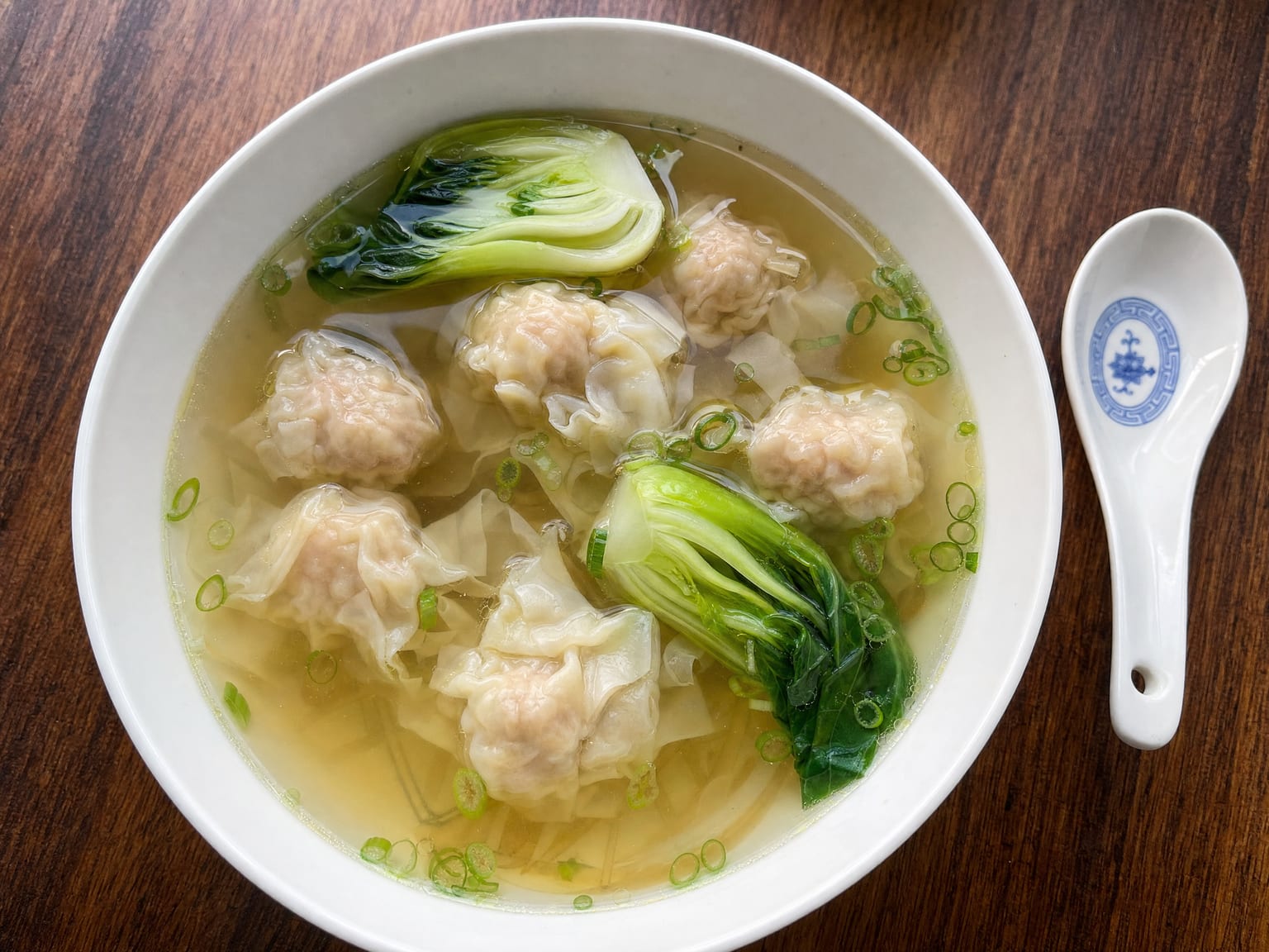 A clear broth bowl with plump pork and prawn wontons, bok choy and sliced scallions