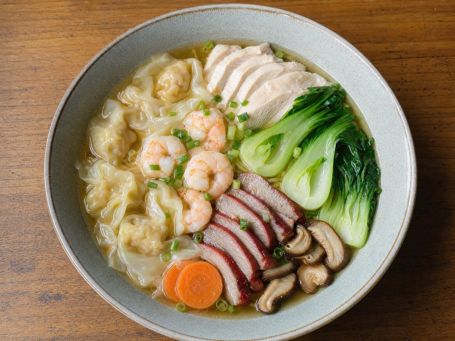 A large bowl of wor wonton soup loaded with wontons, prawns, sliced BBQ pork, chicken and greens in clear broth