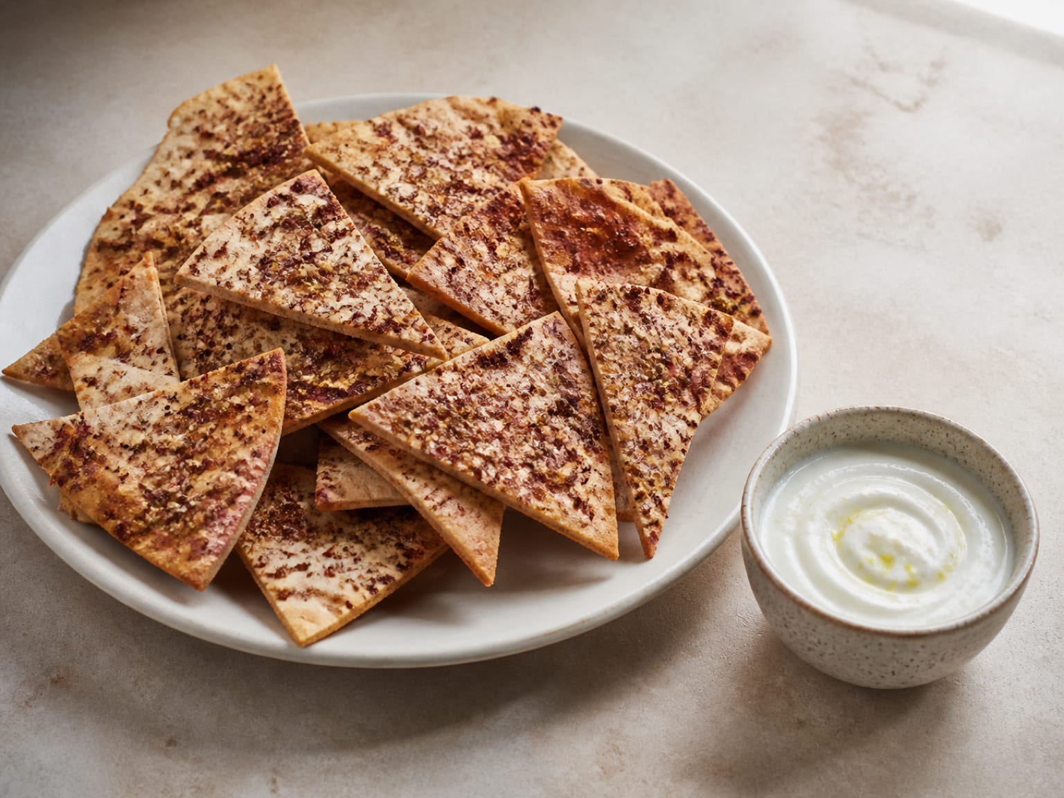 Golden za'atar pita chips beside a small bowl of pale lemon yogurt dip