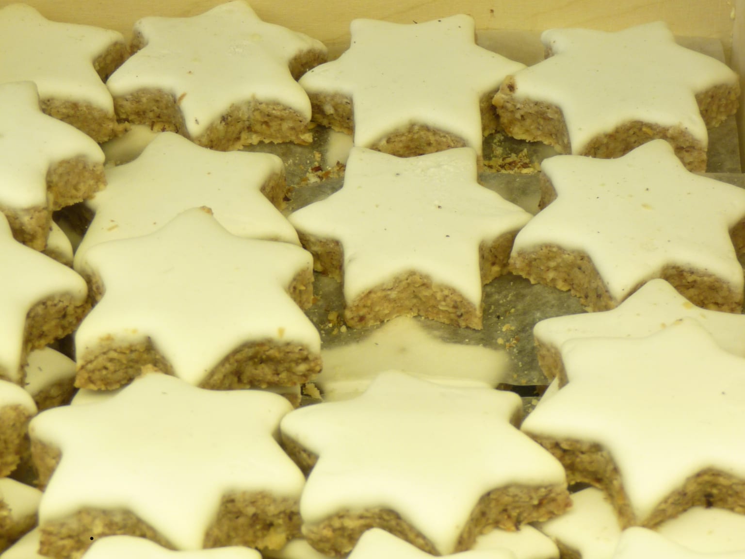 Cinnamon stars with a matte white meringue glaze cooling on a rack over a cream linen cloth, cinnamon sticks and a star cutter to one side in soft natural light